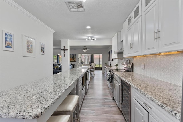 kitchen with a breakfast bar area, white cabinetry, tasteful backsplash, electric range, and beverage cooler