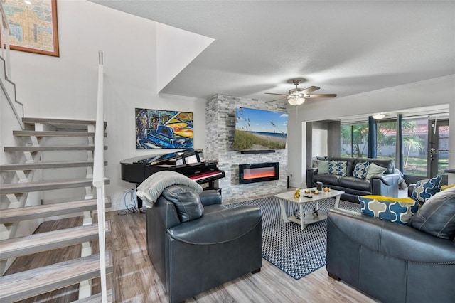 living room with a stone fireplace, light hardwood / wood-style flooring, ornamental molding, and ceiling fan