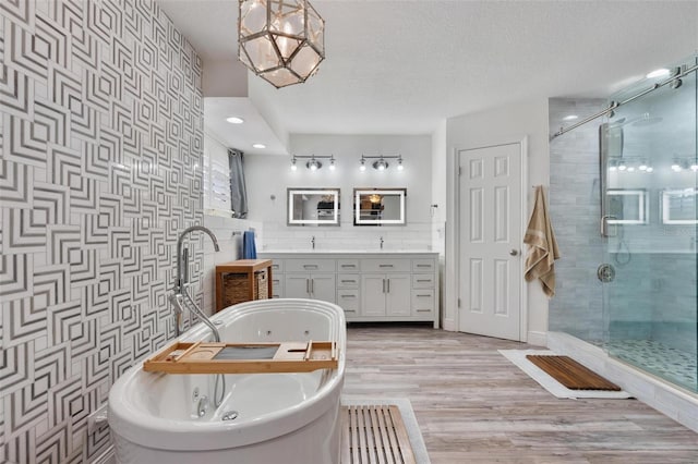 bathroom with shower with separate bathtub, wood-type flooring, tile walls, vanity, and a textured ceiling