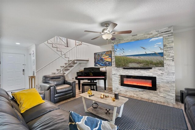 living room featuring a stone fireplace, crown molding, a textured ceiling, hardwood / wood-style flooring, and ceiling fan