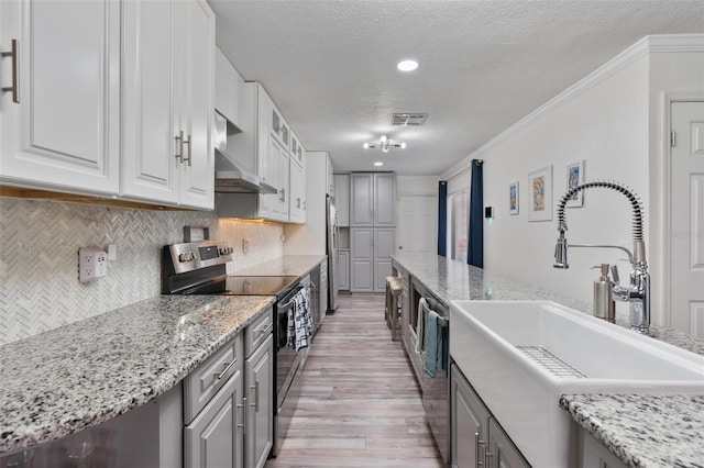 kitchen featuring sink, crown molding, wall chimney range hood, appliances with stainless steel finishes, and white cabinets