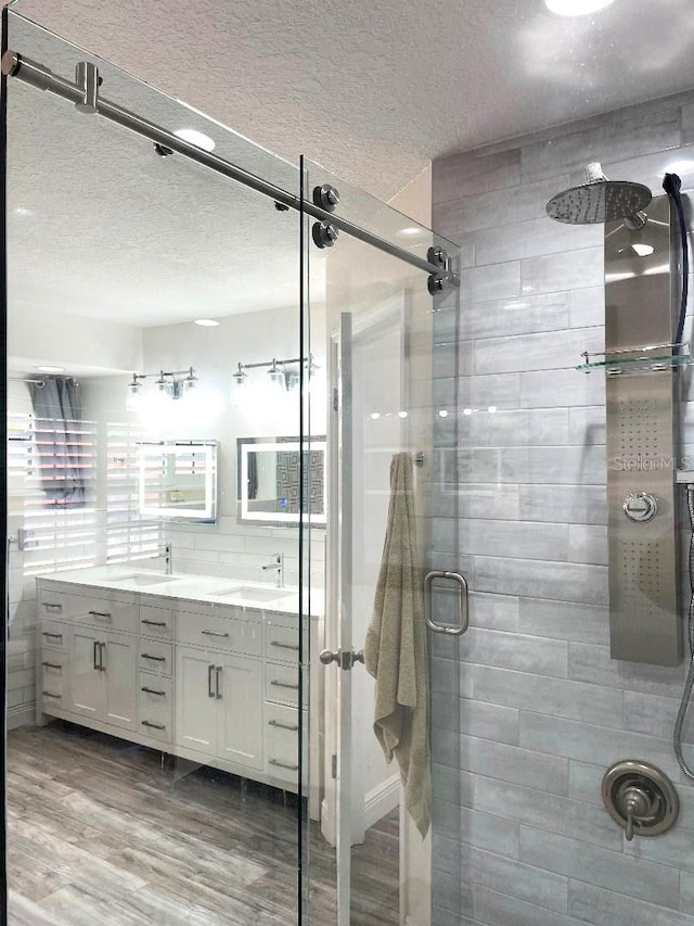 bathroom with hardwood / wood-style flooring, a shower with door, vanity, a textured ceiling, and decorative backsplash