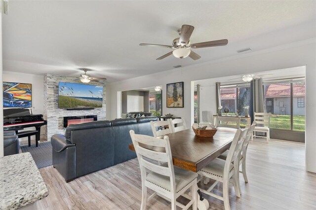 dining room featuring light hardwood / wood-style flooring, a fireplace, ornamental molding, and ceiling fan