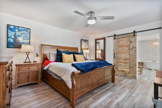 bedroom with crown molding, a textured ceiling, ceiling fan, a barn door, and light hardwood / wood-style floors