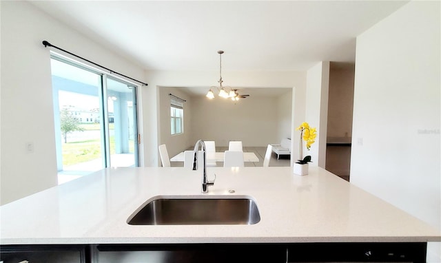 kitchen featuring sink, a chandelier, hanging light fixtures, light stone countertops, and a center island with sink