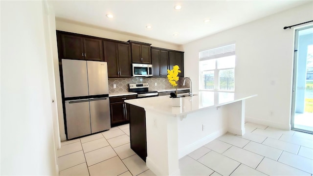 kitchen featuring sink, appliances with stainless steel finishes, backsplash, dark brown cabinetry, and an island with sink