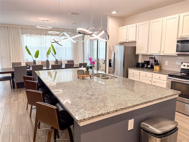 kitchen with an island with sink, appliances with stainless steel finishes, sink, and decorative light fixtures