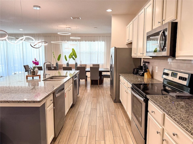 kitchen with sink, a kitchen island with sink, stainless steel appliances, light hardwood / wood-style floors, and decorative light fixtures