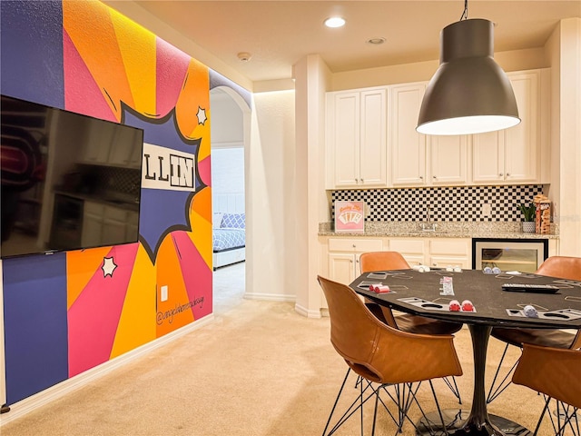 kitchen featuring white cabinets, pendant lighting, light colored carpet, light stone countertops, and backsplash