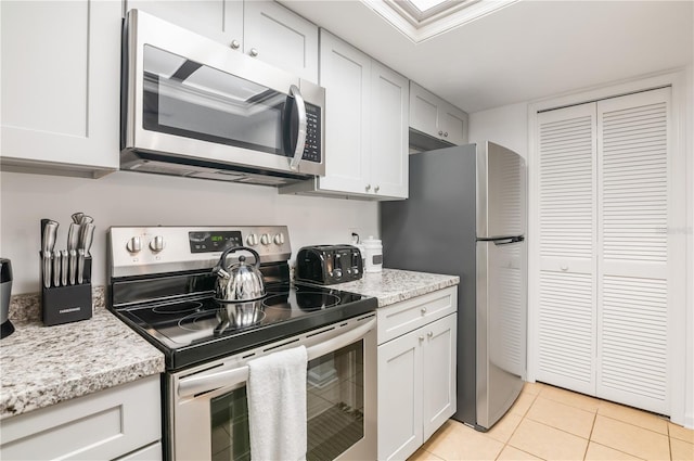 kitchen with white cabinetry, light tile patterned floors, light stone countertops, and appliances with stainless steel finishes