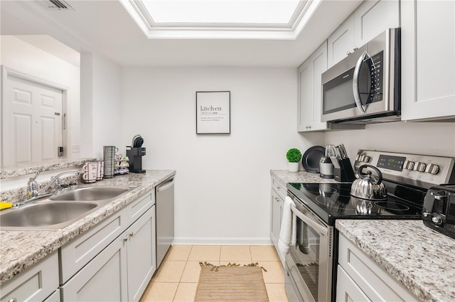 kitchen featuring light tile patterned flooring, appliances with stainless steel finishes, white cabinetry, sink, and light stone counters