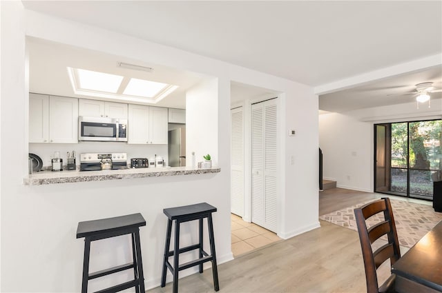 kitchen with a skylight, light stone countertops, kitchen peninsula, and appliances with stainless steel finishes