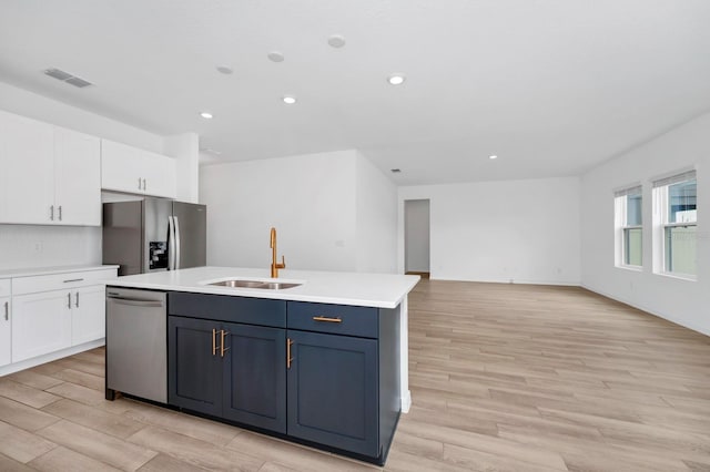 kitchen with sink, appliances with stainless steel finishes, white cabinetry, a center island with sink, and light wood-type flooring