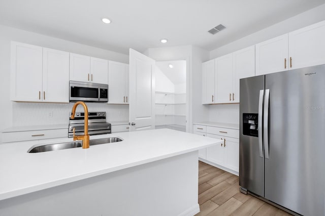 kitchen with stainless steel appliances, white cabinetry, sink, and light hardwood / wood-style floors