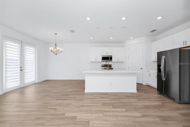 kitchen with hanging light fixtures, stainless steel appliances, an island with sink, white cabinets, and light wood-type flooring