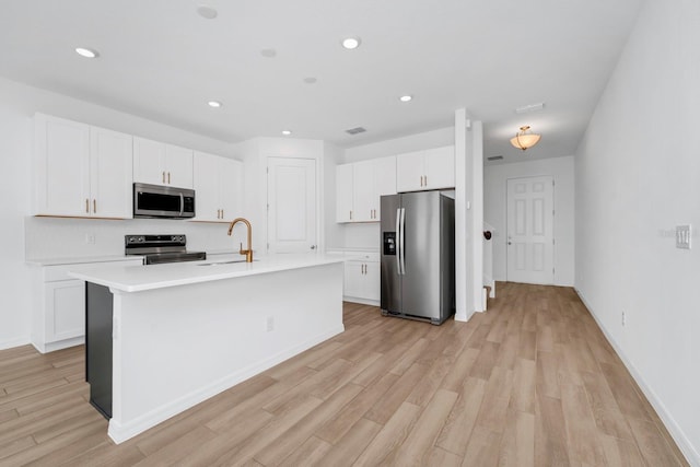 kitchen with white cabinetry, stainless steel appliances, sink, and an island with sink