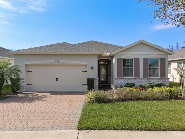 single story home with decorative driveway, roof with shingles, stucco siding, a garage, and stone siding