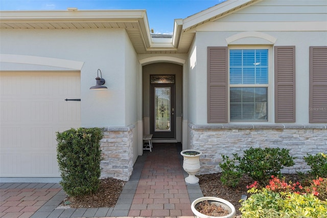 entrance to property featuring a garage, stone siding, and stucco siding