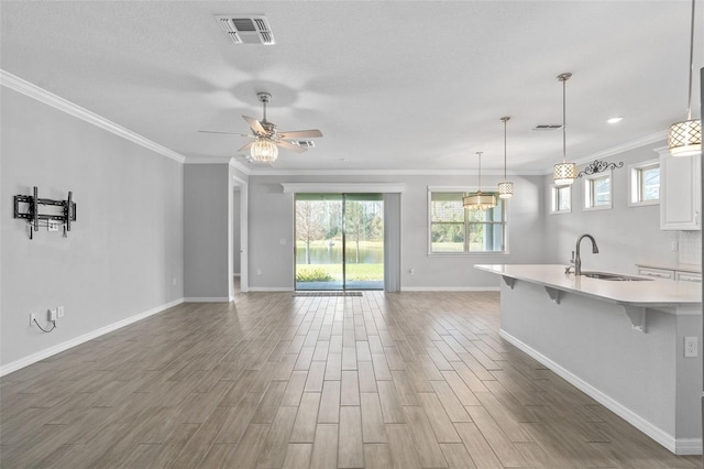 unfurnished living room featuring sink, a textured ceiling, ornamental molding, ceiling fan, and hardwood / wood-style floors