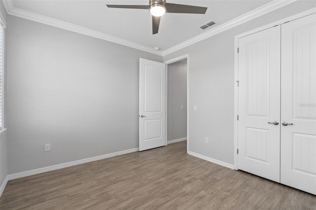 unfurnished bedroom with wood finished floors, visible vents, baseboards, ornamental molding, and a closet