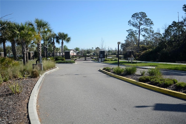 view of street featuring street lights, curbs, a gated entry, and a gate