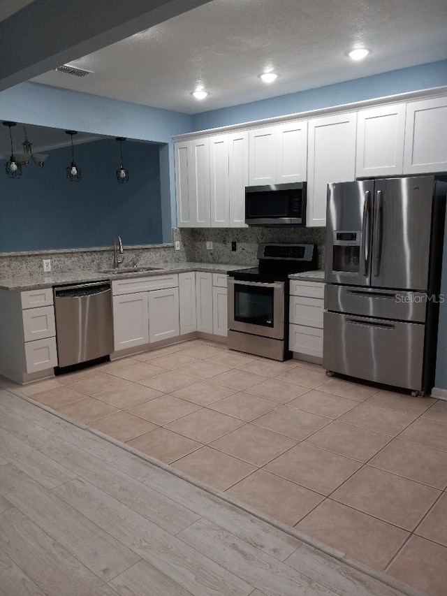 kitchen with sink, white cabinetry, stainless steel appliances, light stone countertops, and backsplash