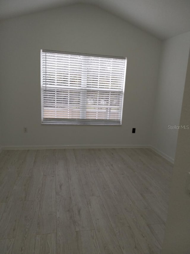 spare room with vaulted ceiling and light wood-type flooring