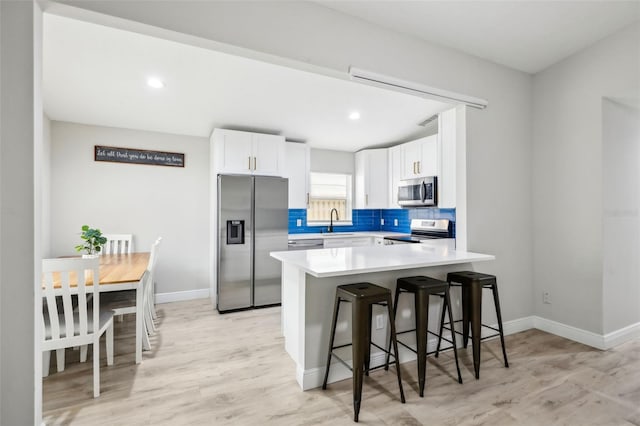 kitchen featuring appliances with stainless steel finishes, a breakfast bar, white cabinets, and decorative backsplash