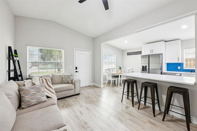 living room with ceiling fan, vaulted ceiling, and light hardwood / wood-style flooring