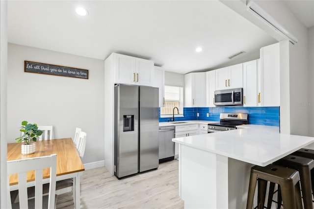 kitchen with sink, a breakfast bar area, appliances with stainless steel finishes, white cabinets, and decorative backsplash