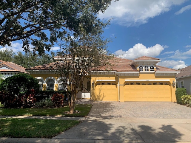 mediterranean / spanish home with stucco siding, an attached garage, a tile roof, and driveway