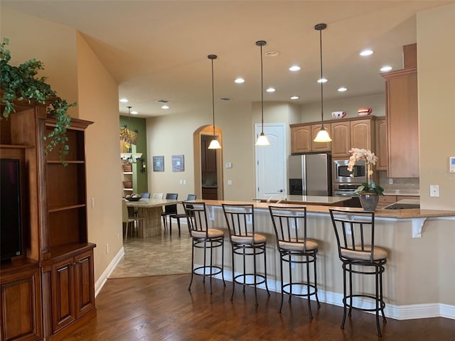 kitchen with a kitchen bar, stainless steel appliances, arched walkways, a peninsula, and hanging light fixtures