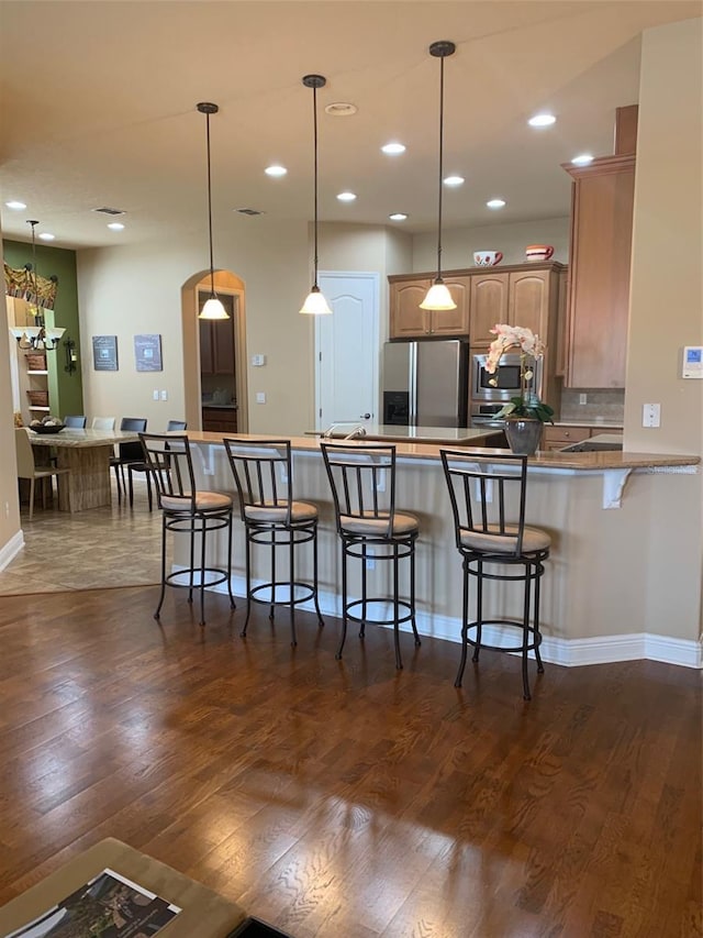 kitchen featuring tasteful backsplash, pendant lighting, a kitchen breakfast bar, stainless steel refrigerator with ice dispenser, and dark wood-style floors