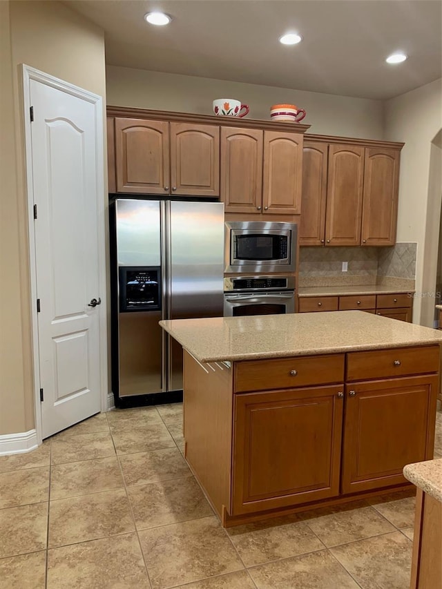 kitchen with a center island, light stone counters, decorative backsplash, recessed lighting, and appliances with stainless steel finishes
