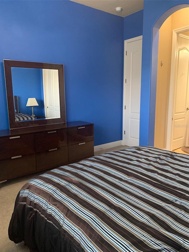 bedroom featuring arched walkways, baseboards, and carpet