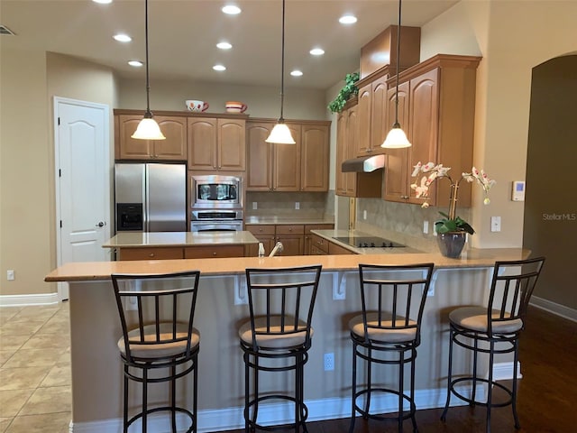 kitchen with under cabinet range hood, backsplash, appliances with stainless steel finishes, a peninsula, and light countertops