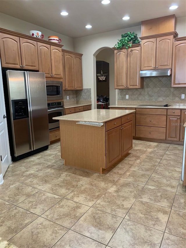 kitchen featuring a center island, under cabinet range hood, light stone counters, appliances with stainless steel finishes, and arched walkways