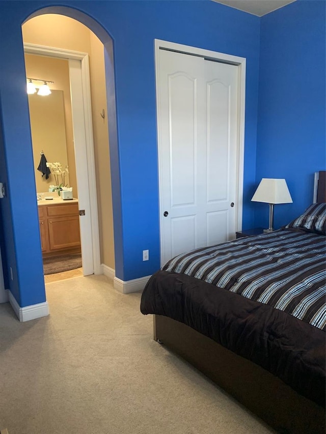 bedroom featuring a closet, light colored carpet, arched walkways, and baseboards