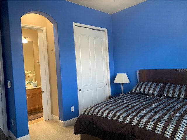 bedroom featuring baseboards, arched walkways, light colored carpet, and a closet