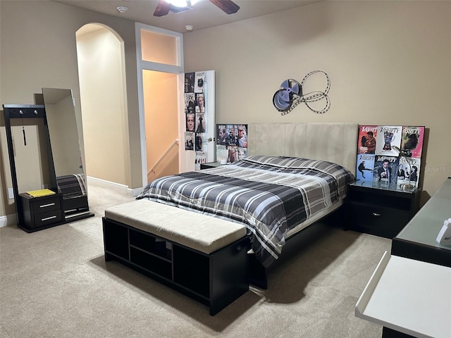 bedroom featuring baseboards, arched walkways, light colored carpet, and a ceiling fan