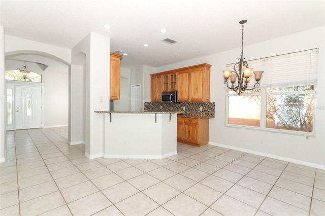 kitchen featuring a kitchen breakfast bar, kitchen peninsula, a notable chandelier, pendant lighting, and backsplash