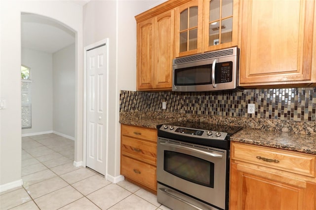 kitchen with stainless steel appliances, tasteful backsplash, light tile patterned floors, and dark stone counters