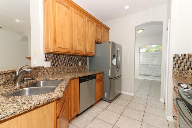 kitchen with sink, light tile patterned floors, appliances with stainless steel finishes, stone countertops, and decorative backsplash