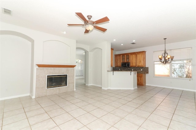 unfurnished living room featuring a tiled fireplace, ceiling fan with notable chandelier, and light tile patterned floors