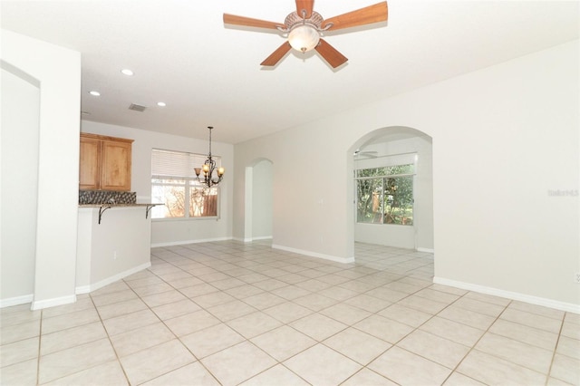 tiled empty room with ceiling fan with notable chandelier