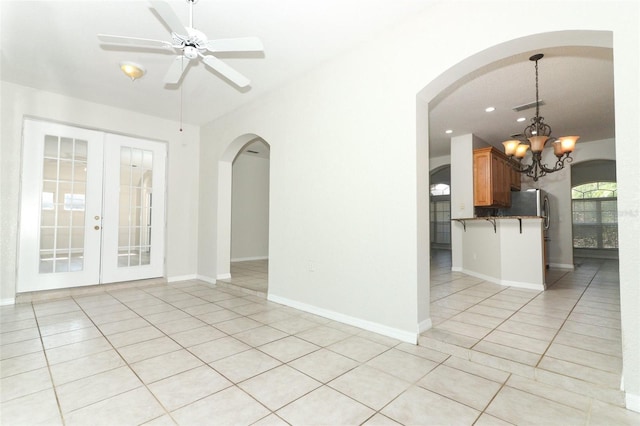 tiled spare room with ceiling fan with notable chandelier and french doors