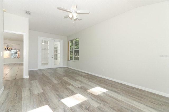 spare room featuring french doors, ceiling fan with notable chandelier, and light wood-type flooring