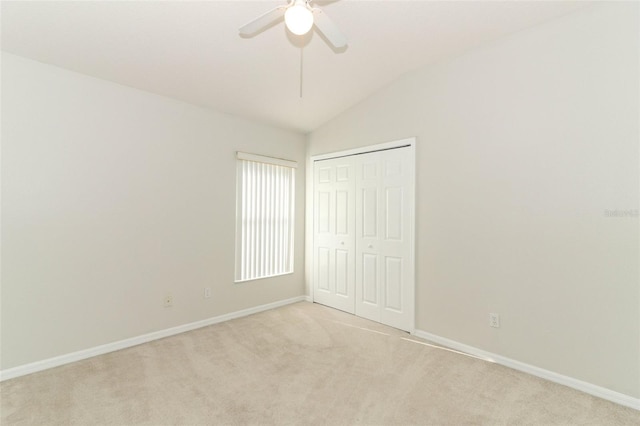 unfurnished bedroom featuring ceiling fan, light colored carpet, vaulted ceiling, and a closet