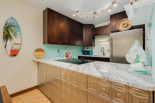 kitchen with sink, light tile patterned floors, stainless steel refrigerator, black electric stovetop, and light stone countertops