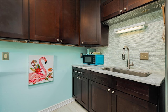 kitchen featuring dark brown cabinets, light stone countertops, sink, and decorative backsplash